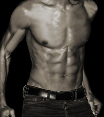 Sexy young male in jeans showing abs on black background. Image black and white.