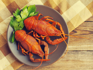 Boiled crawfishes in a round brown plate on a cloth on a wooden background, top view