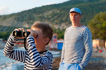 boy in garrison cap and striped vest standing near the sea with