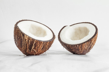 Two fresh halves of a coconut on a soft white glossy surface