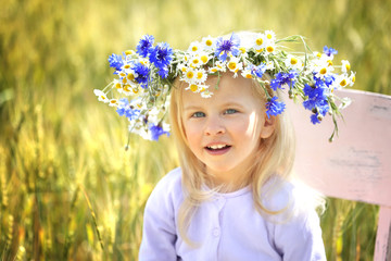 Little blonde girl with wreath in the field