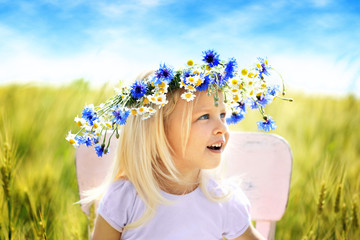 Little blonde girl with wreath in the field