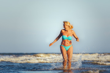 Fototapeta premium The girl in a swimsuit walking on the waves of the sea