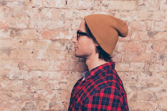Side-view photo of hipster with hat near brick wall