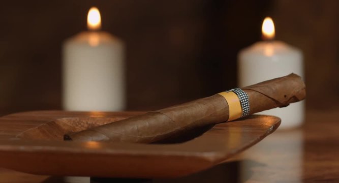 4K Slider Fahrt von einer kubanischen Zigarre in einem Holzaschenbecher mit Kerzen im Hintergrund zu einem offenen Zigarrenkasten auf einem  Holztisch.