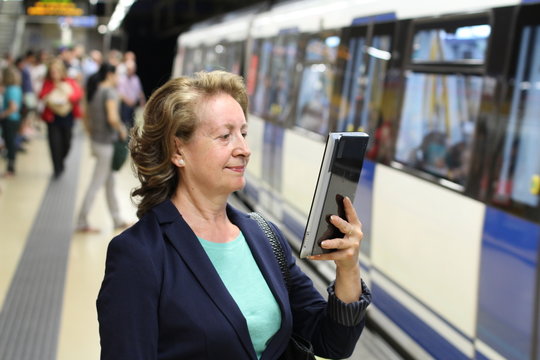 Smiling mature woman using eBook in subway while waiting train at metro station