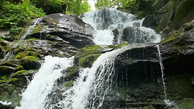 Cascade waterfall splash on stones in forest among mountains. Slow motion.