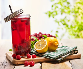 On wooden boards is red ice cold drink glasses jar and metal cap with raspberry lemon cocktail . Country ice cold drink two hundred and five with raspberry clay bowl outdoor