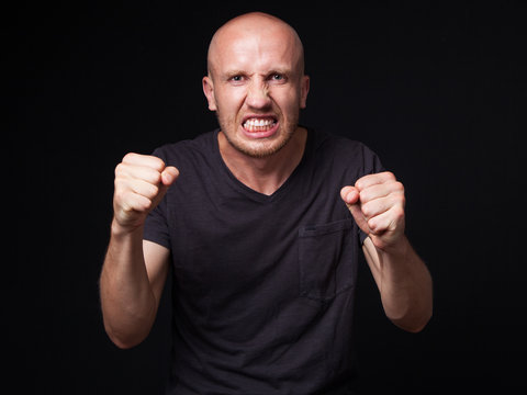 Close up portrait of an angry bald man, shaking his fists, black background