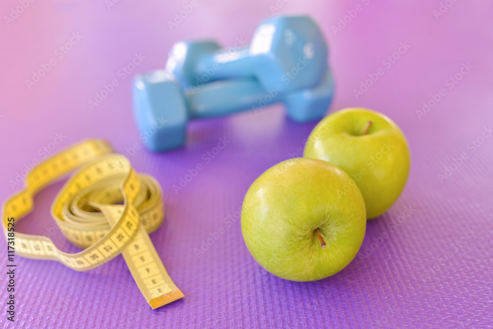 Wall mural healthy lifestyle concept - green apple with dumbbells and yellow measuring tape