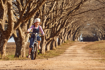 Young girl riding her bicycle bike down dirt road tree lined ave