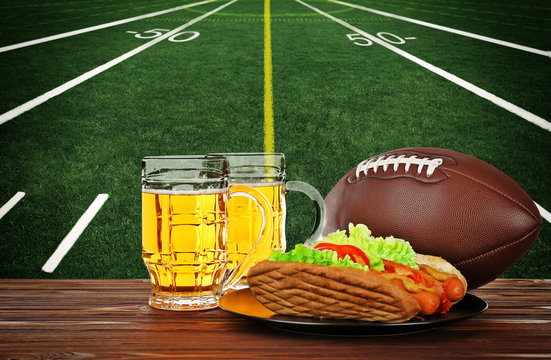Two glass of beer, ball and snack on football field background