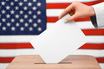 Hand putting down voting paper into a ballot box on American flag background