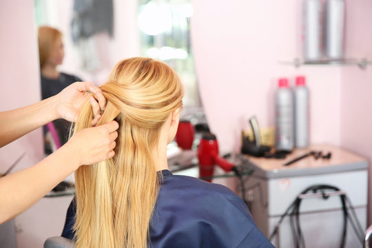 Hairdresser braiding woman's hair in hairdressing salon