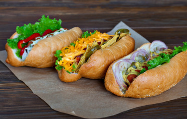 Assorted three hot dogs with ketchup, mustard and salad on a wooden background