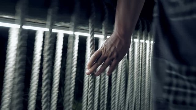 A man is walking alone at night on a bridge while touching the ropes. Walking alone at night can be dangerous. One has to be aware of their surrounding.