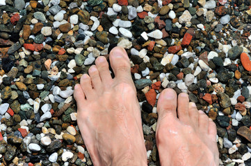 Men's feet on sea pebbles in the water