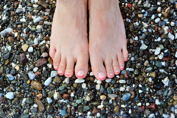 Girl's leg on colorful pebbles on the beach by the sea