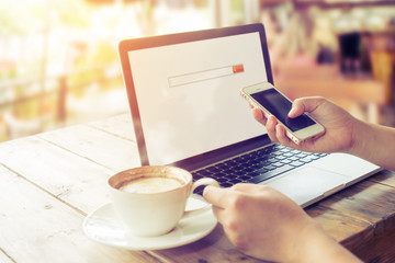 Side view of beautiful young hipster woman's hands busy working on her laptop, female using cell telephone sitting at wooden table in a coffee shop - retro filter effect and vintage color style