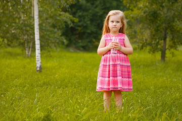 Child holding glass water. Girl in pink dress in summer