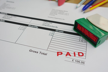       Person Hand Holding Rubber Stamp Over Red Paid Stamp On Invoice     