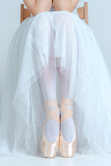 Professional ballerina sitting with her ballet shoes on the gray background