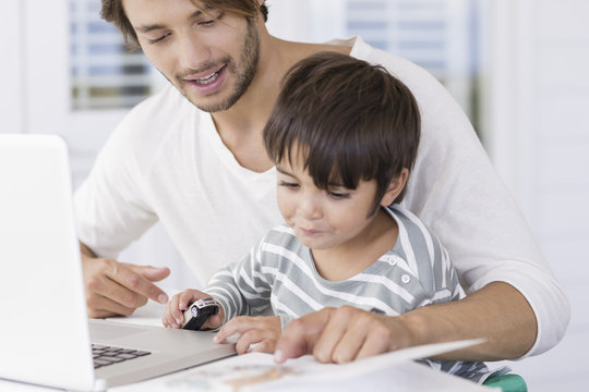 Father and son looking at map on book while using laptop at home