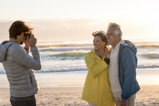 Young man taking a picture of his parents with camera on the beach