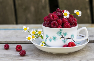 Cup with ripe raspberry on a wooden substrate with chamomile flowers 