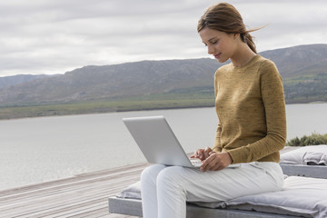 Happy young woman using a laptop at lakeshore
