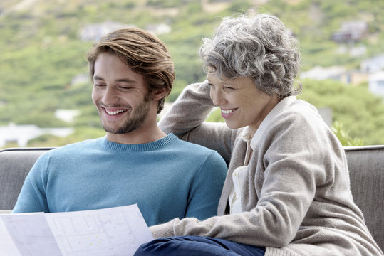 Happy mother with her adult son reading a blueprint outdoors