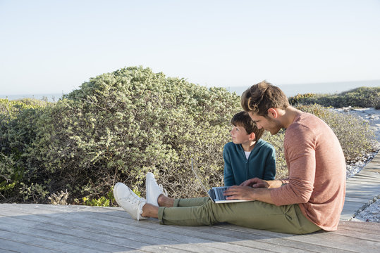 Father and son using a laptop on boardwalk