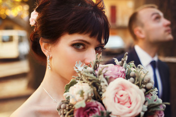 Blue-eyed brunette bride hides her face behind a wedding bouquet
