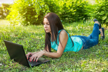 Young woman lying on the grass, using laptop and typing