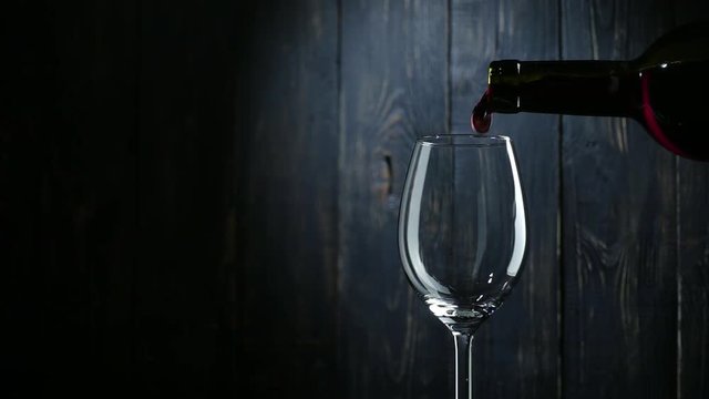 Pouring red wine into glass over dark wooden background. Slow motion.

