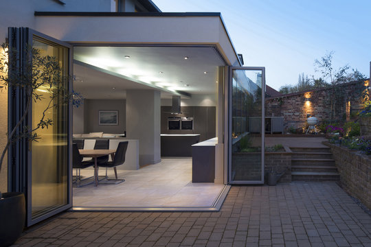 Kitchen and dining areas seen through open bi-fold doors from the patio and garden at dusk. A modern family home.