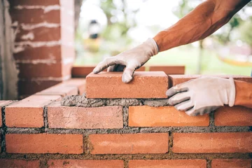 Photo sur Aluminium Mur de briques professional construction worker laying bricks and building barbecue in industrial site. Detail of hand adjusting bricks