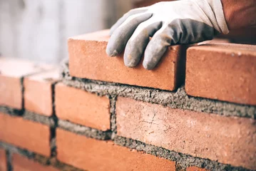 Photo sur Plexiglas Mur de briques Gros plan sur un maçon industriel installant des briques sur un chantier de construction