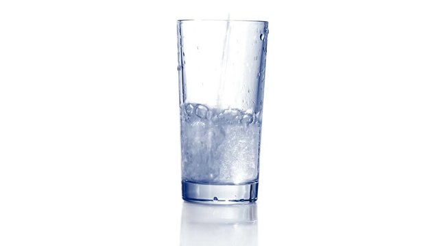 Filling empty glass with carbonated water, dropping ice cubes. Bubbles come out. Close up, extreme close up. 4K Ultra HD.
