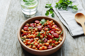 Chickpeas with chorizo in a clay bowl on the table close-up