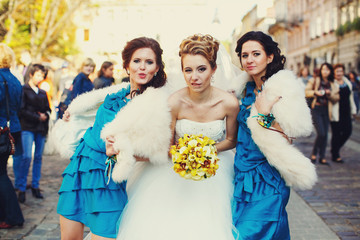 Bride bites her lips posing with funny bridesmaids on the street