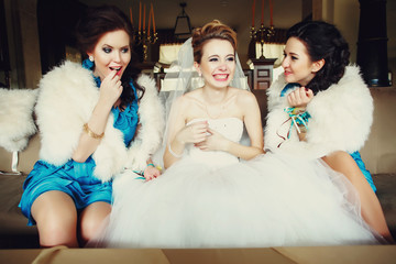 Bride sits on the beig couch surrounde by bridesmaids in white f