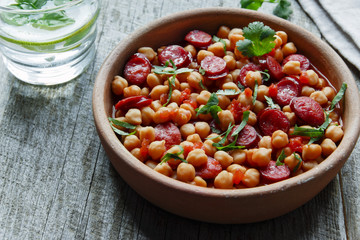 Chickpeas with chorizo in a clay bowl on the table close-up