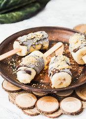 frozen bananas on a stick with chocolate and nuts, dark clay pla