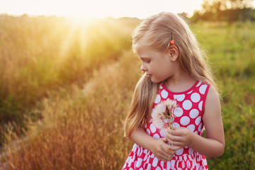 Little girl with dandelion on a meadow in the sunset.