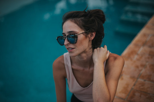 Brunette woman in sunglasses with hair in bun at pool