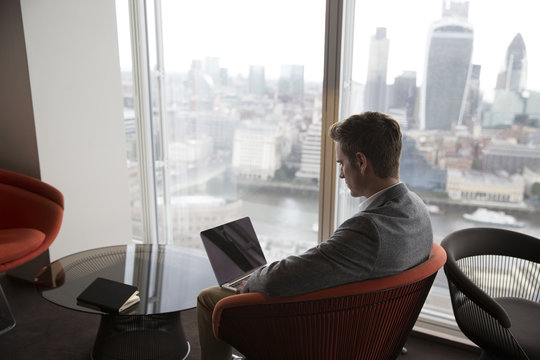 Businessman Sits In Chair With Laptop In High Rise Office