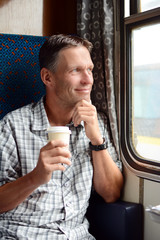 Man in the train looking out of the window and holding hot drink.
