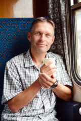 Man in the train looking out of the window and holding hot drink.