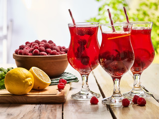 Wooden boards are ice cold beverage glasses with red berry raspberry and slice lemon cocktail . Alcohol country cocktail beverage number three hundred five with raspberry basket. Cocktail on outdoor.